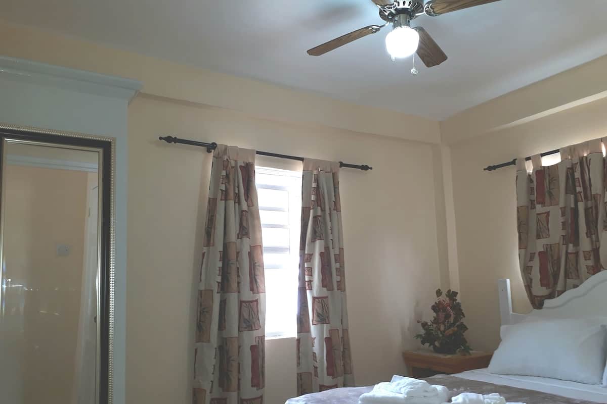 Un dormitorio con cama, cortinas, ventilador de techo y mesita de noche con una planta.