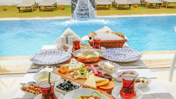 Un espace de restauration aménagé au bord de la piscine, avec une table dressée pour un repas, entourée de chaises longues et agrémenté d’une cascade.
