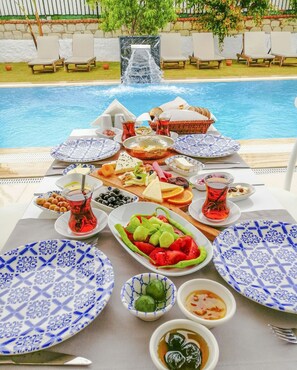A poolside dining setup with a table set for a meal, surrounded by lounge chairs and a waterfall feature.