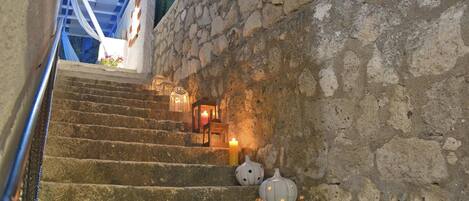A stone staircase leading to a room with a bed and a nightstand, decorated with pumpkins and a lit candle.