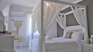 Un lit à baldaquin avec des rideaux blancs, une table de chevet avec une lampe et une chaise agrémentée d’une décoration murale en macramé.