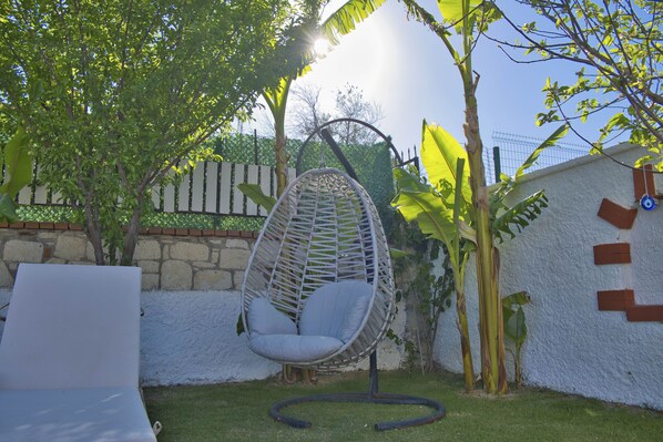 A hanging chair in a garden with a white wall and a stone wall in the background.