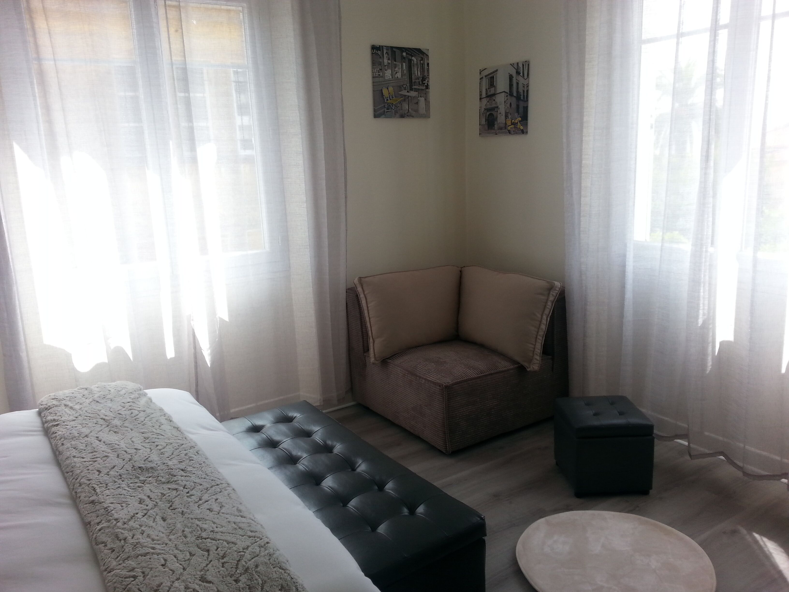A modern bedroom with a large bed, a cushioned bench, a small ottoman, and two framed pictures on the wall.