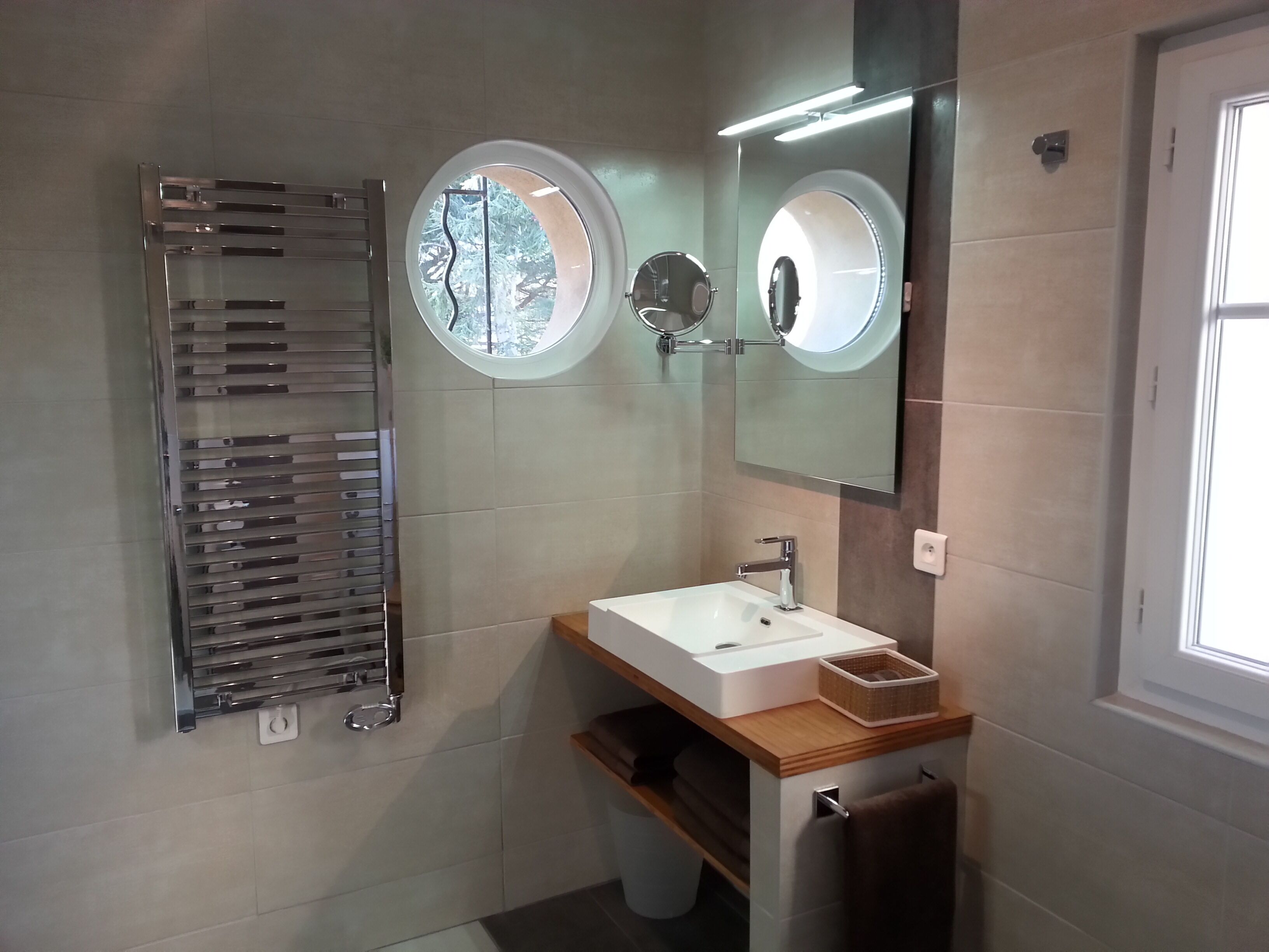Un baño moderno con toallero integrado, un espejo redondo y un lavabo blanco.