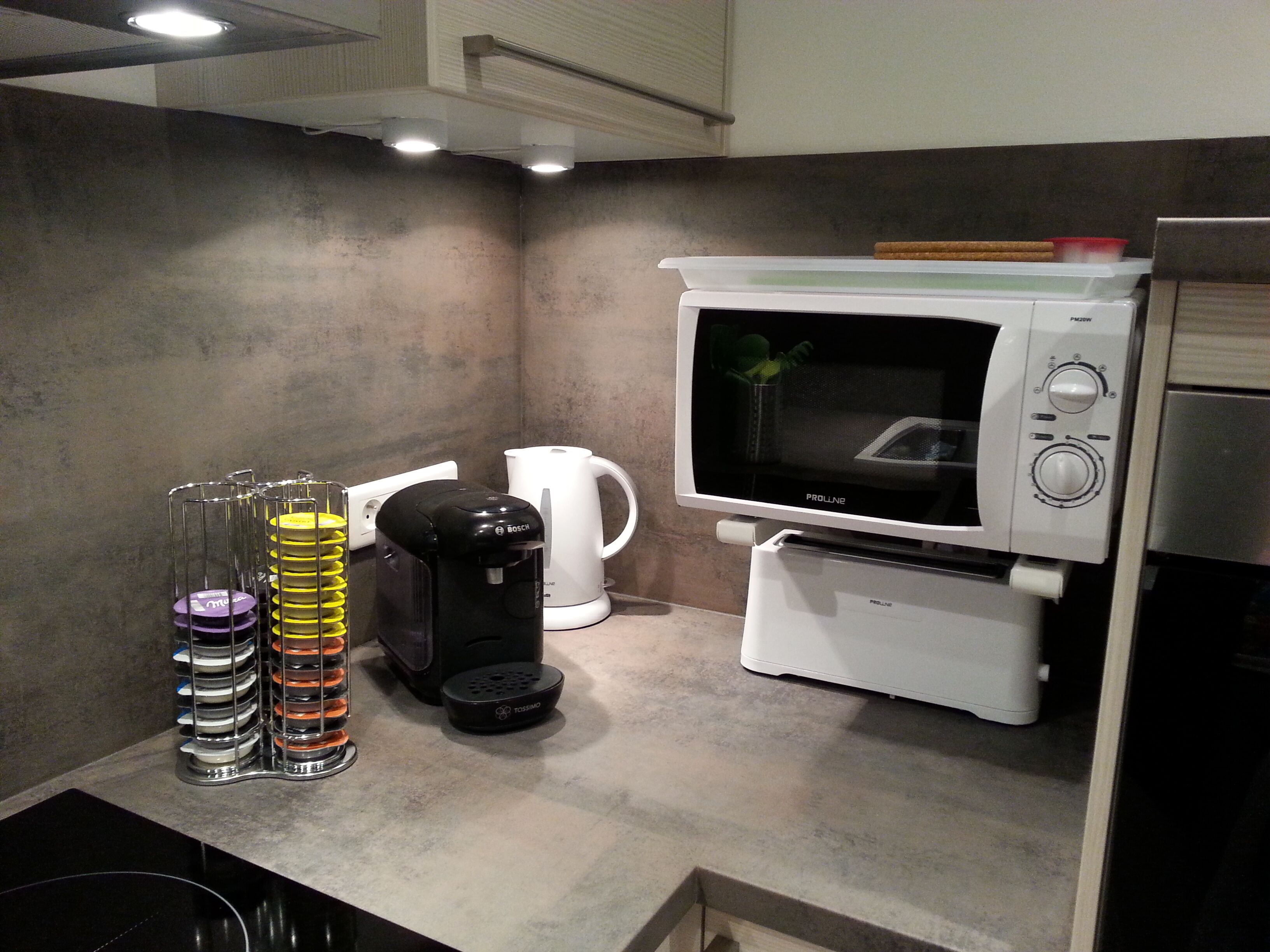 A compact kitchen with a microwave, coffee maker, and stacked dishes.