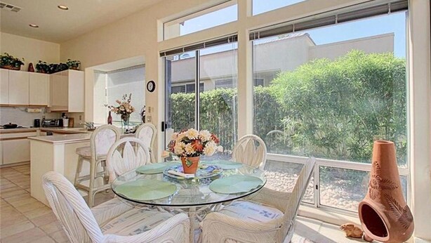 Una cocina moderna con armarios blancos, una mesa de comedor de vidrio con sillas, y vistas a zonas verdes.