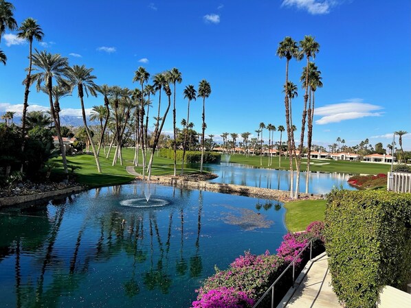 A golf course with a pond, palm trees, and a clear blue sky. - Indian Wells 3 bedroom 3 bath Condo in exclusive Desert Horizons Country Club (Indian Wells)