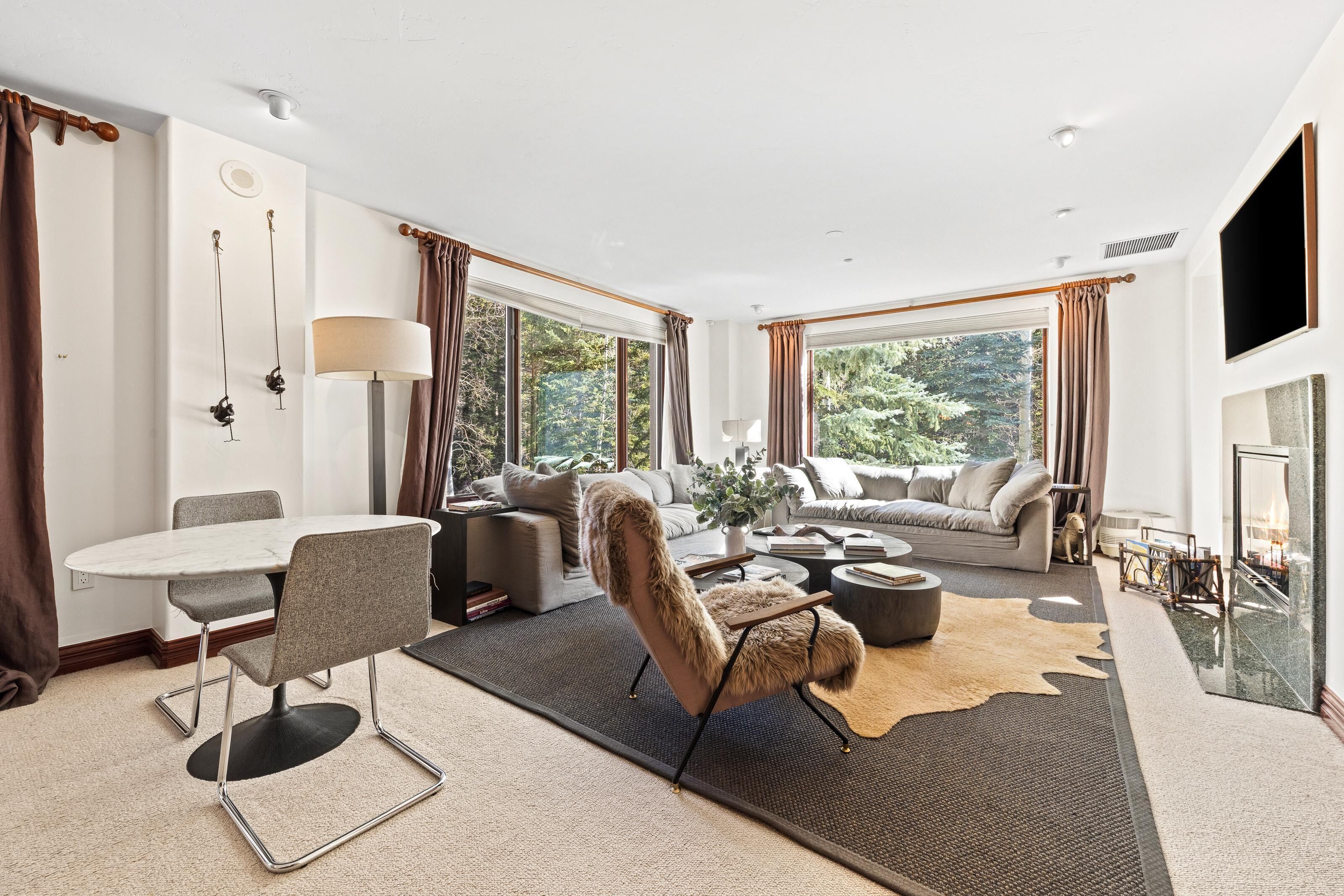 Ein modernes Wohnzimmer mit einem runden Tisch, zwei Sofas, einem Fellstuhl und einem Kamin.