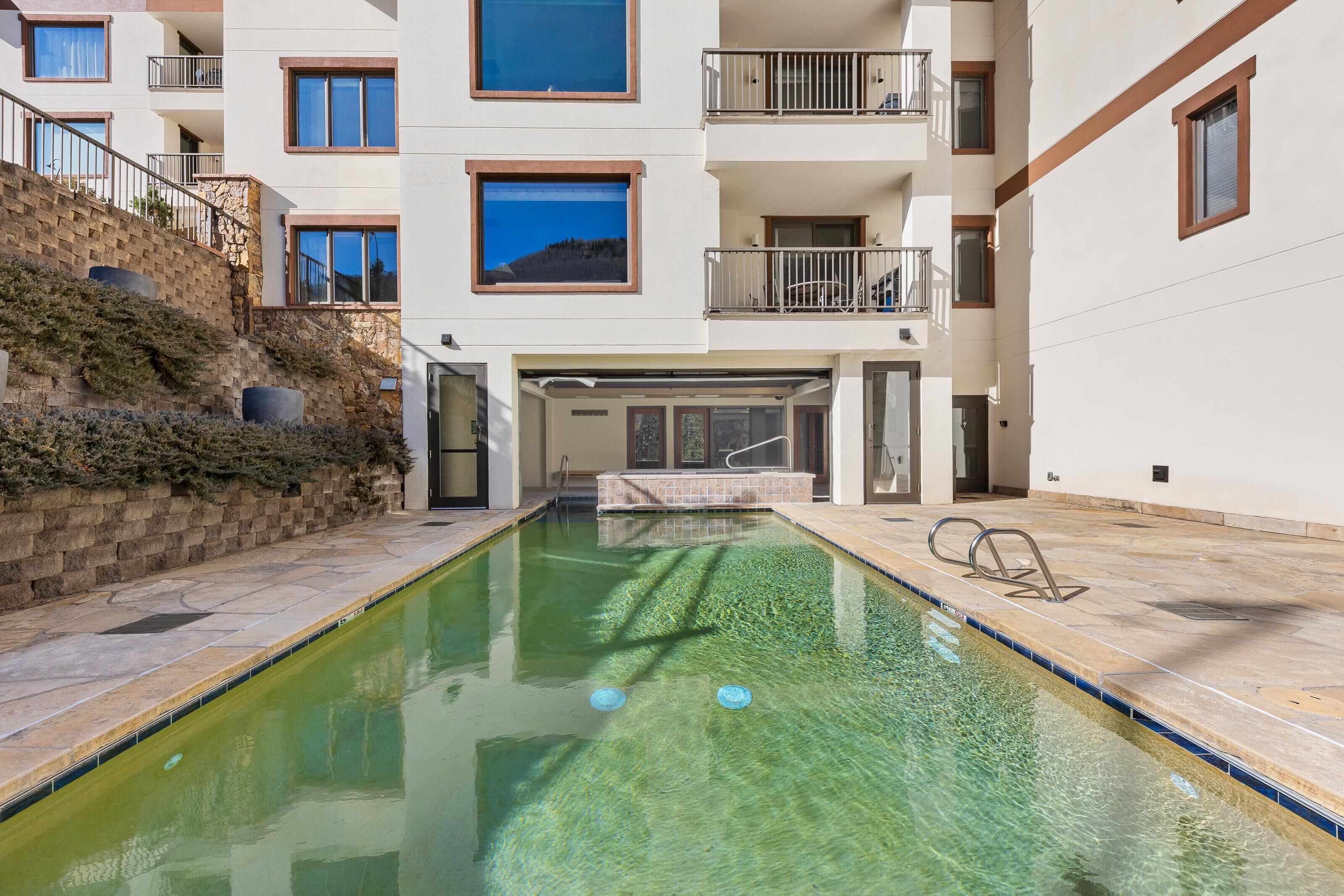 A swimming pool with a stone wall and a building with balconies and windows.