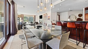 Un comedor moderno con una mesa y sillas de vidrio, luces colgantes y vistas al exterior.