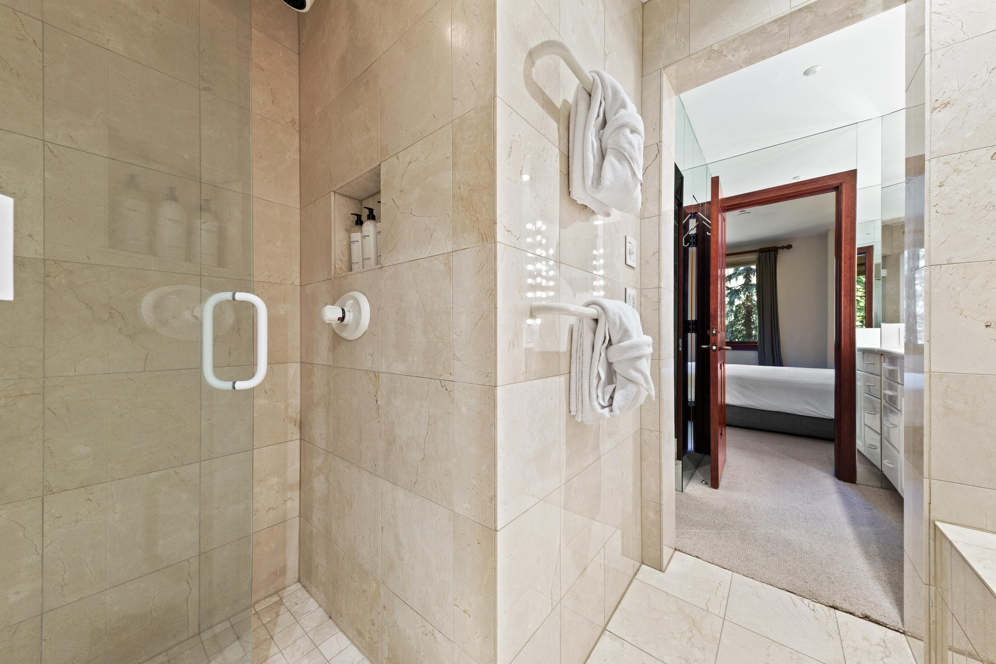 Un baño moderno con cabina de ducha de vidrio, toallero blanco y lavamanos a la vista.