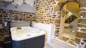 A modern bathroom with a stone wall, a hot tub, and a wooden archway leading to another room. - La Cazette (Severac-d'Aveyron)