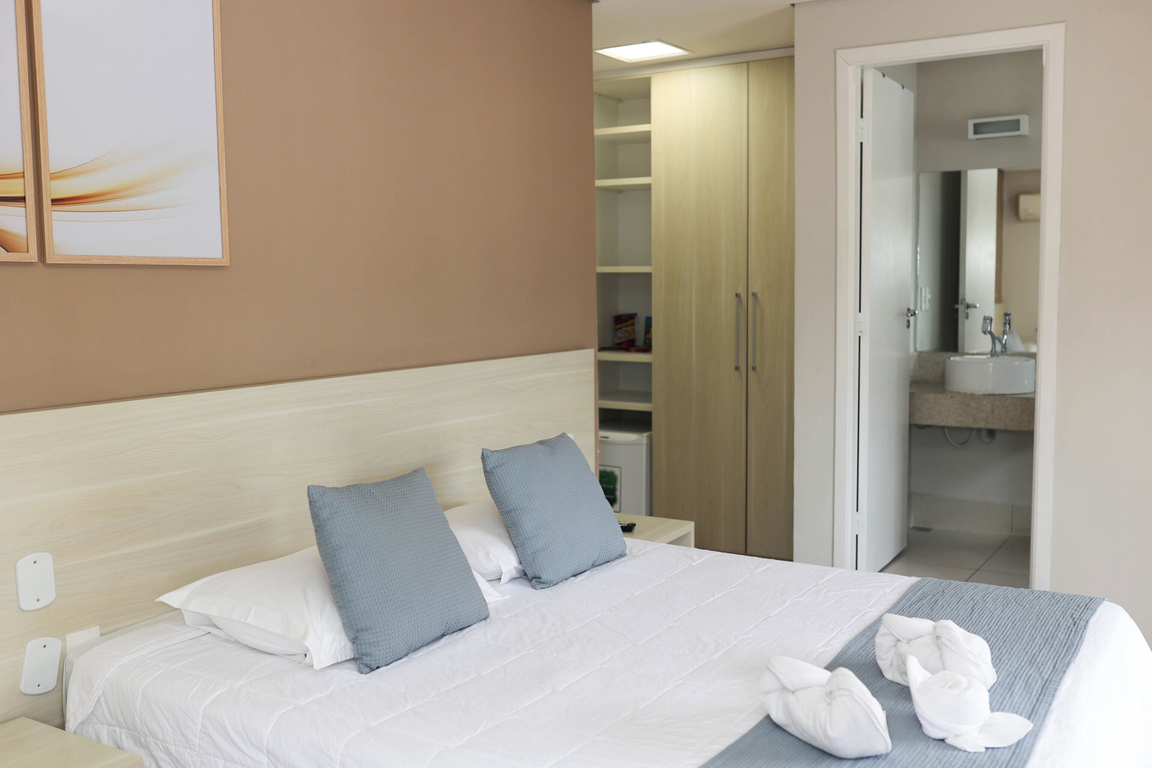Habitación de hotel con cama, almohadas, mesita de noche, armario y baño visible a través de una puerta abierta.
