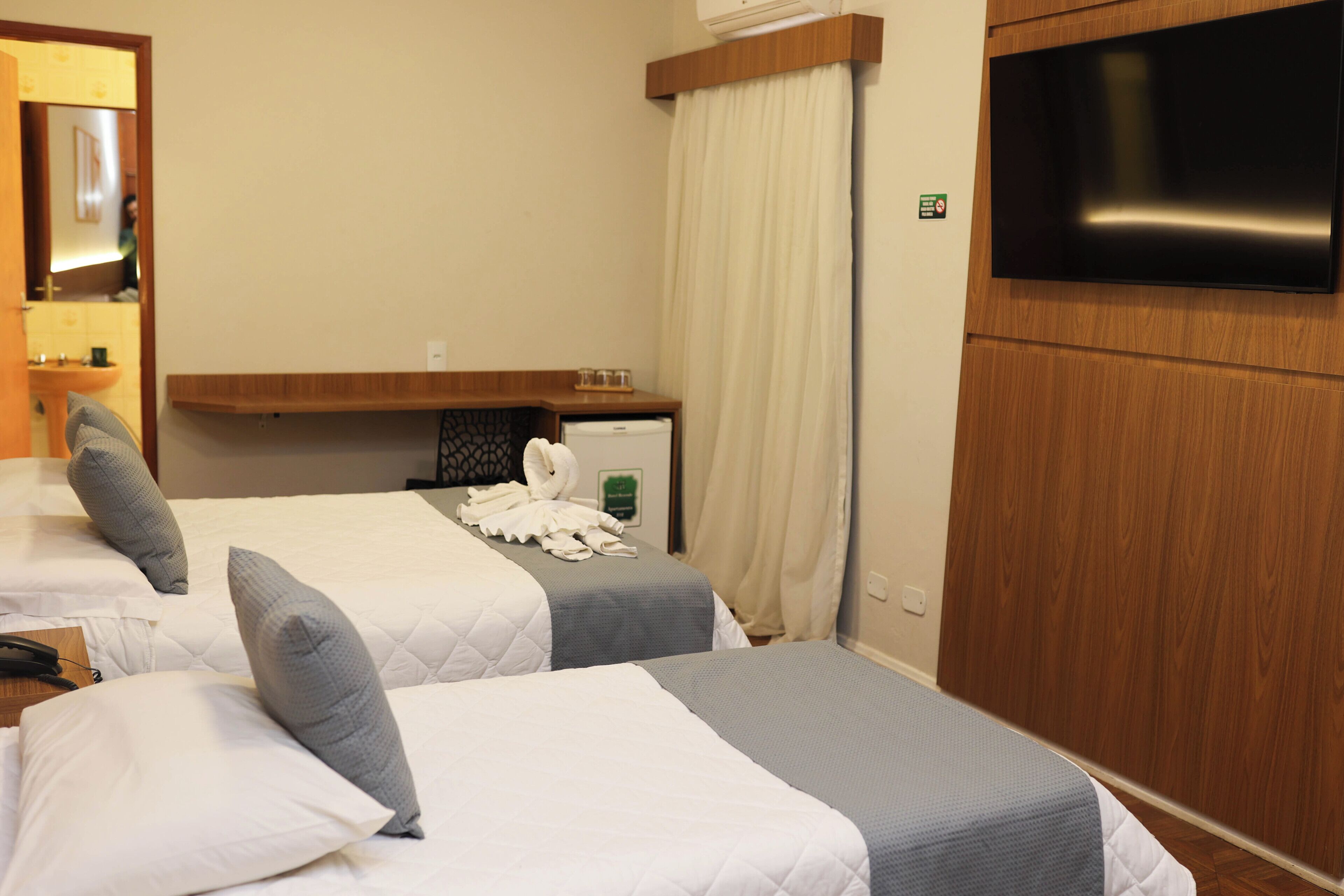 Een hotelkamer met twee bedden, een televisie, een klein tafeltje met glazen en een handdoekrek.