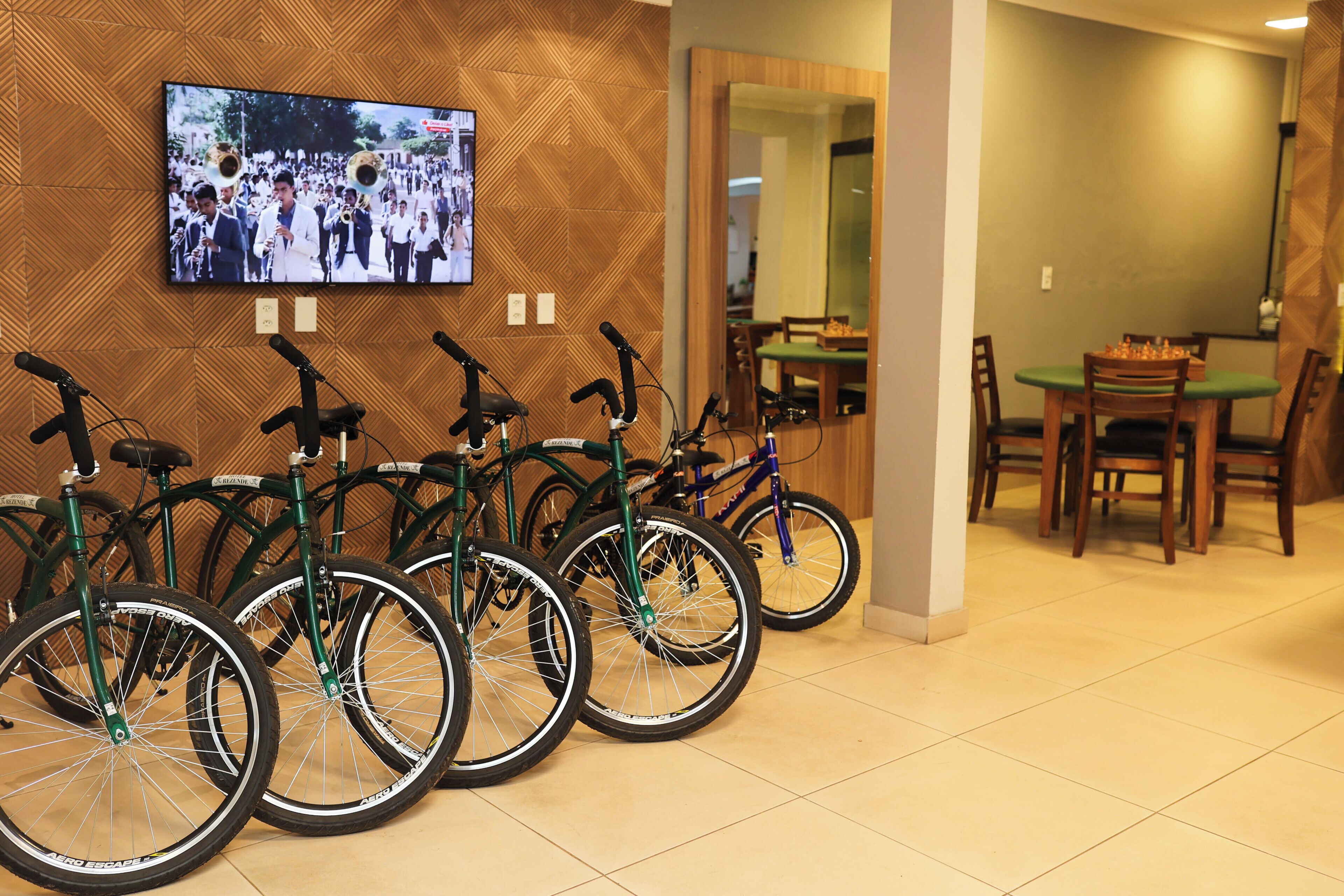 A room with bicycles parked against a wall, a television mounted on the wall, and a dining area in the background.
