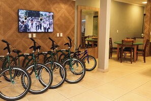 Une pièce où des vélos sont appuyés contre un mur, un téléviseur fixé au mur et, au fond, un coin repas.