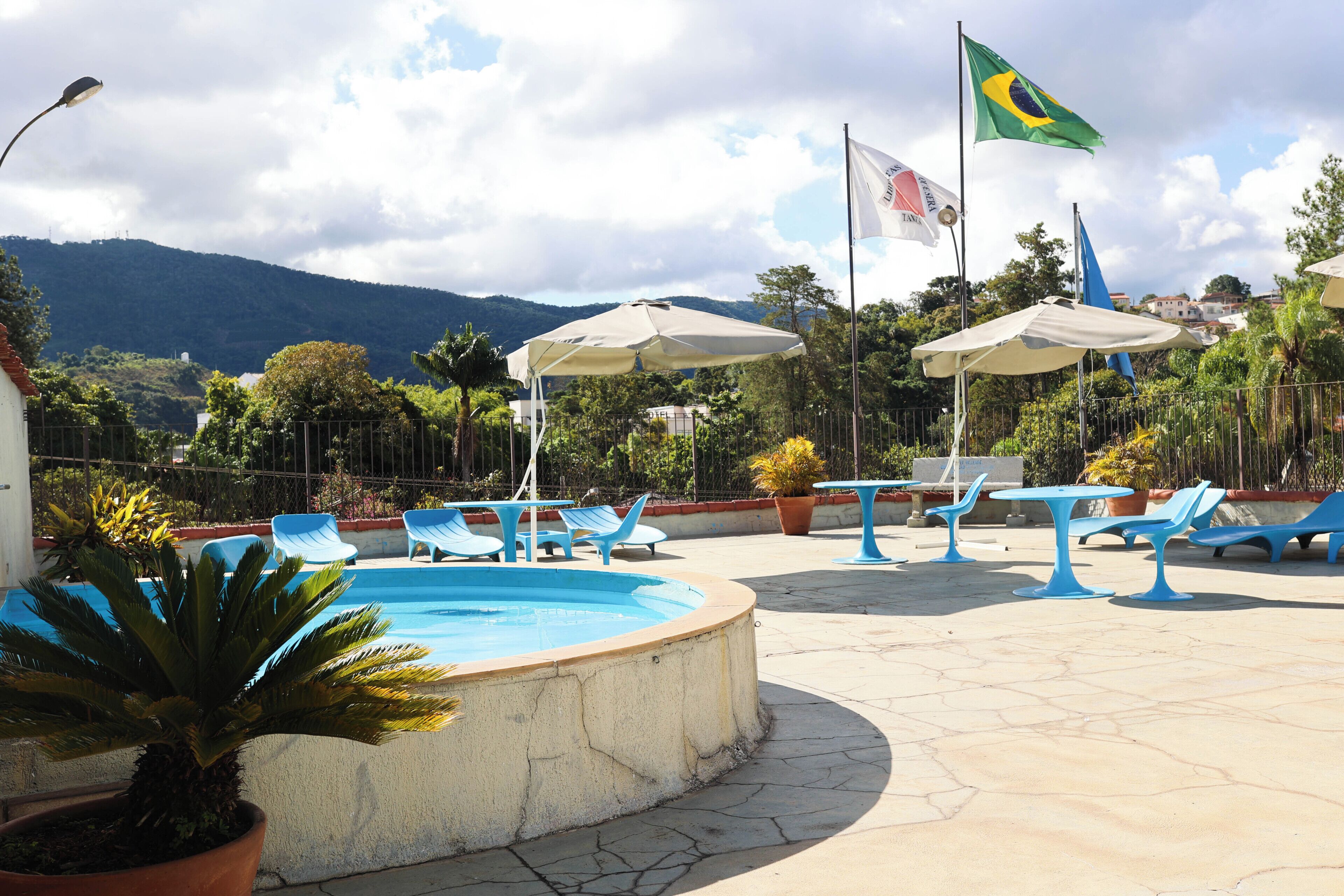 Zona de piscina con sillas, sombrillas, banderas y montañas al fondo.