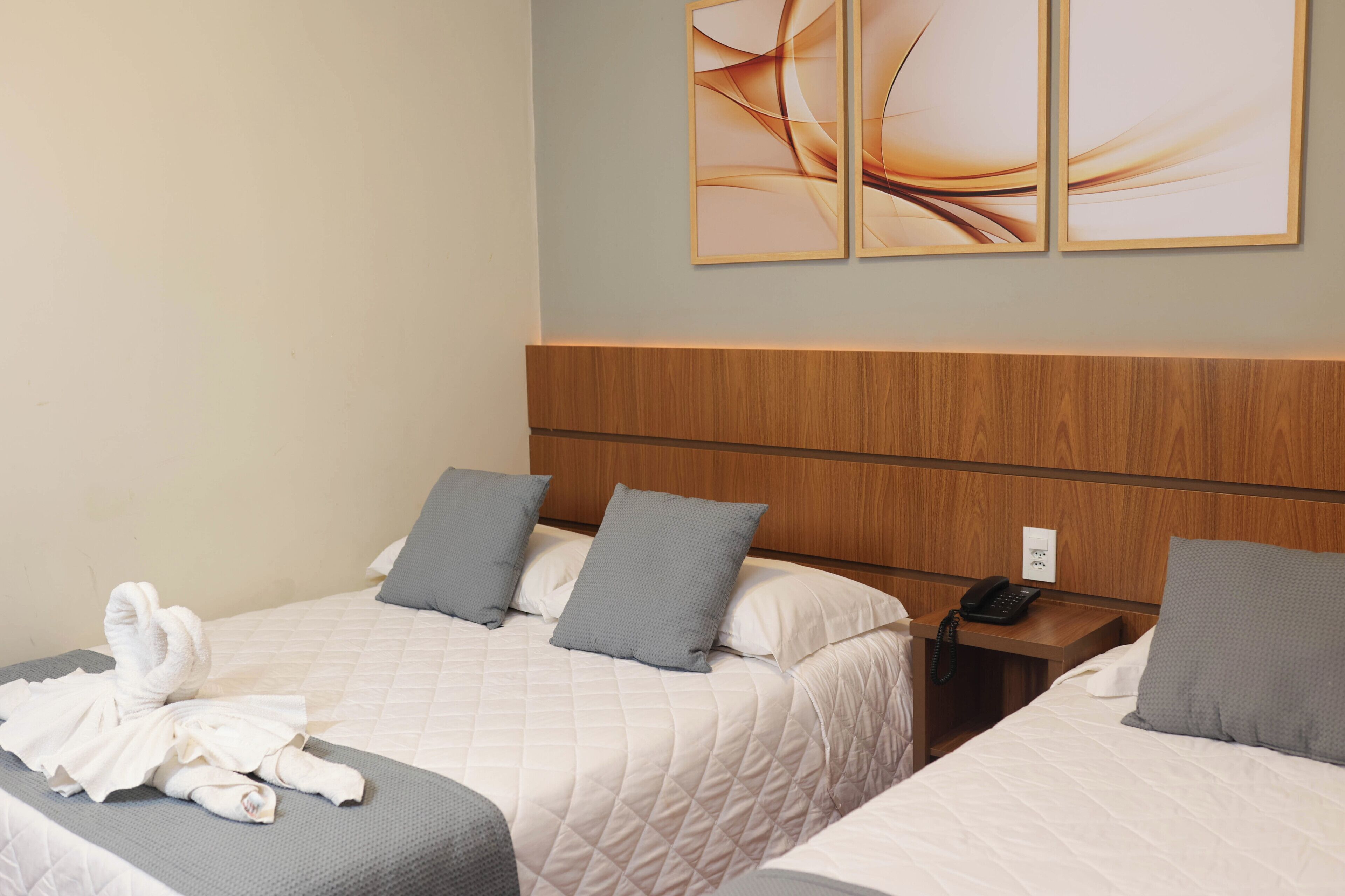 A hotel room with two beds, a wooden headboard, a bedside table with a phone, and artwork on the wall.