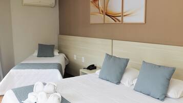 Quarto de hotel com duas camas, mesa de cabeceira com telefone e ar condicionado fixado na parede.