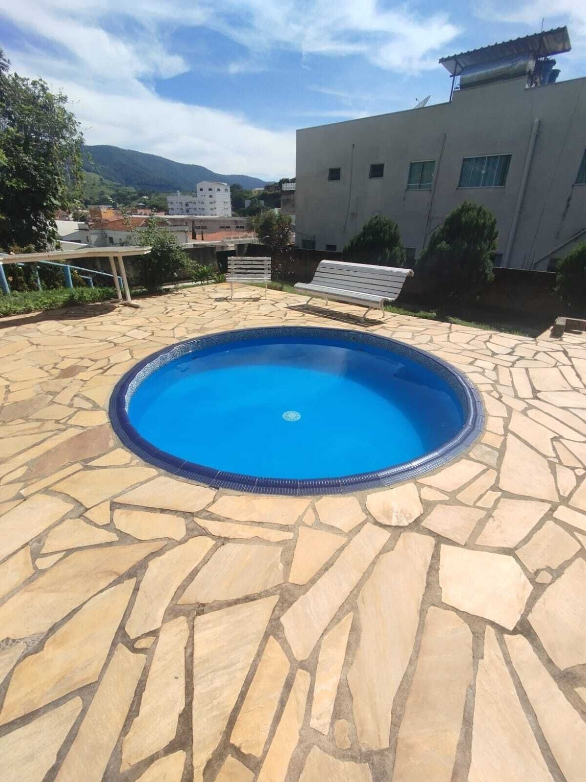 A swimming pool with a stone deck, surrounded by a building and greenery.