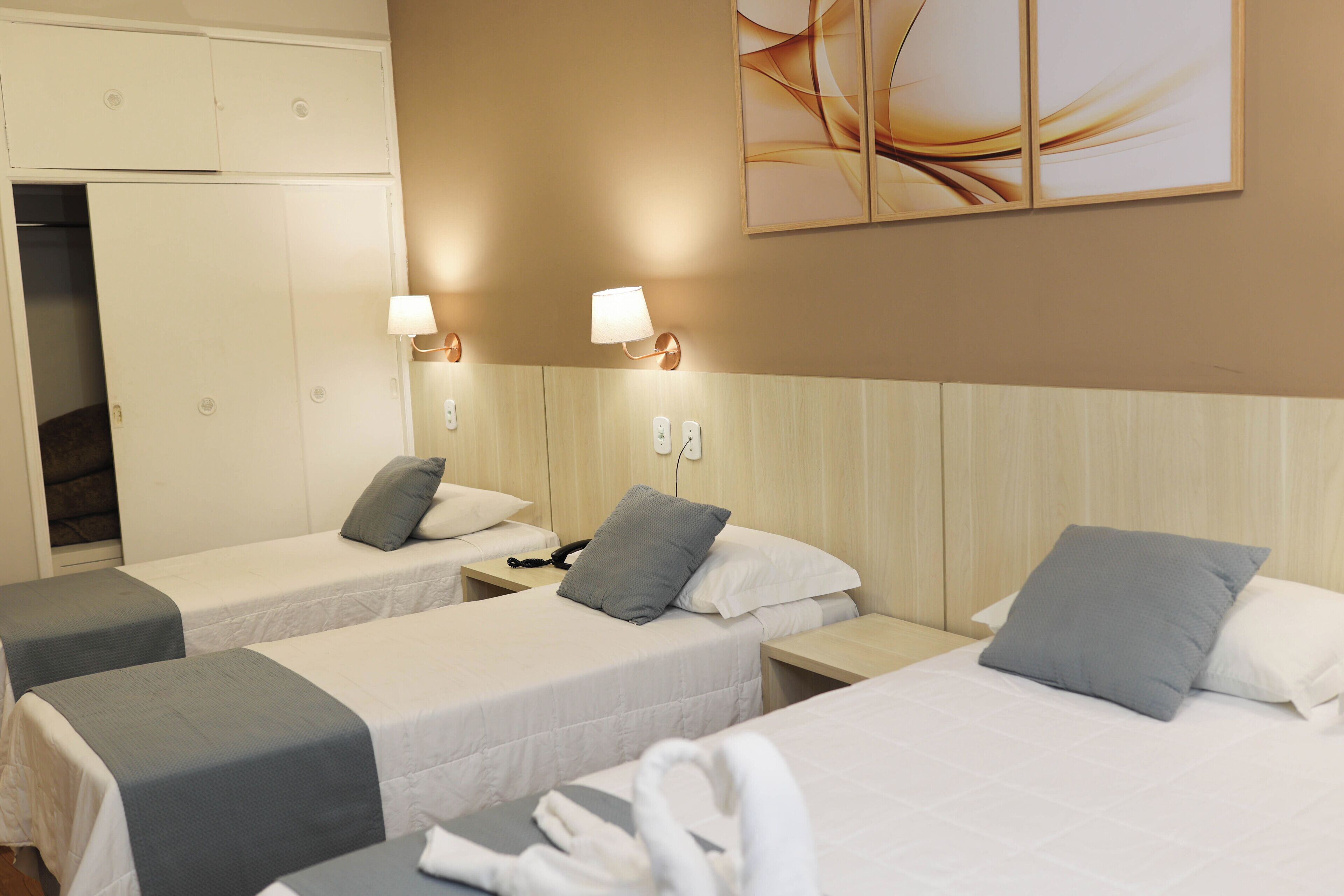 A hotel room with two single beds, a wooden headboard, bedside lamps, a telephone, and a wall-mounted artwork.