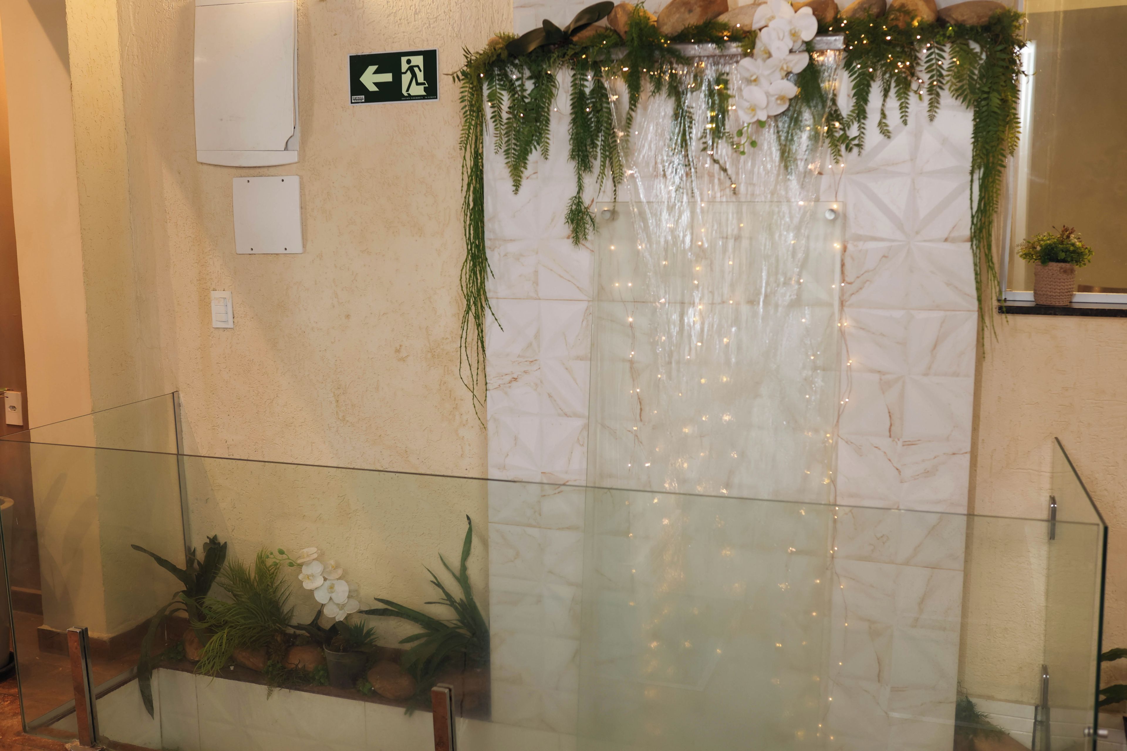 A wall with a waterfall feature, a glass railing, and potted plants.
