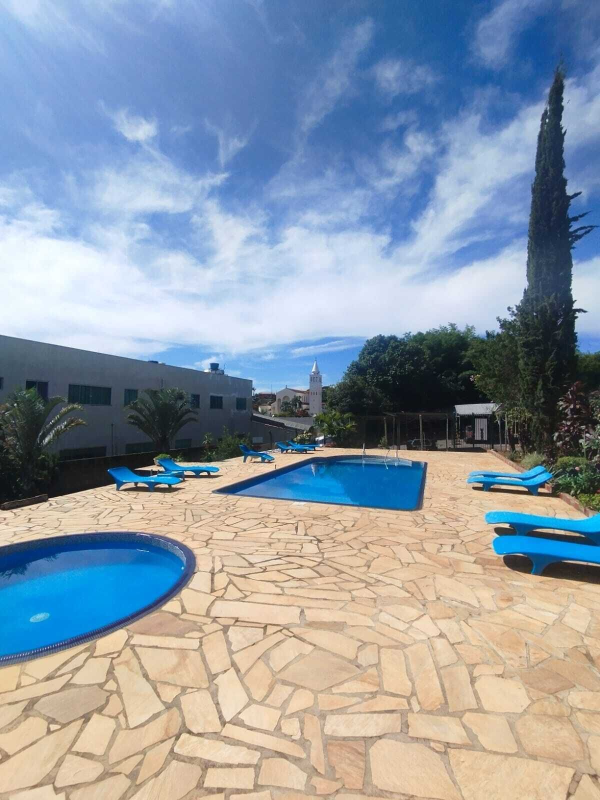 A pool area with stone flooring, blue lounge chairs, and a tall tree.