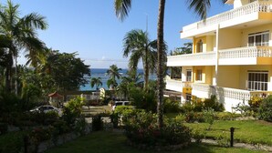 Um hotel com varanda de dois andares, vista para o oceano e um jardim bem cuidado com palmeiras e flores.