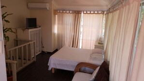 Quarto de hotel com cama, televisão em um móvel, planta em vaso e janela com cortinas.