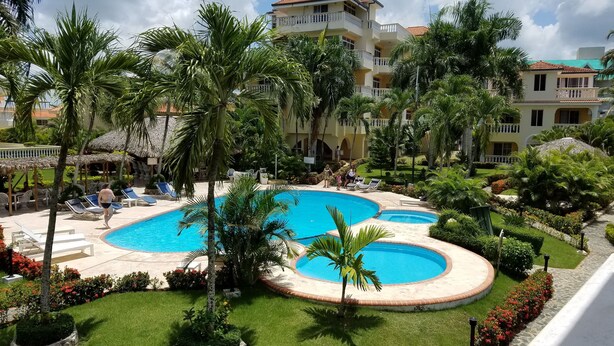 Um resort com uma piscina grande, palmeiras e um edifício com varandas.