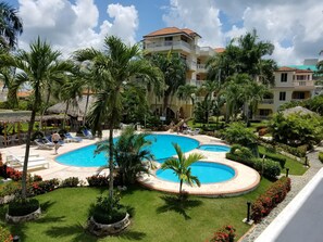 A resort with a large pool, palm trees, and a building with balconies. - Las Palmeras I Mamajo & Riki (Boca Chica)