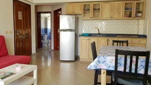 Cozinha compacta com armários de madeira, geladeira e área de refeições com mesa e cadeiras.
