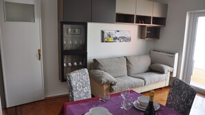A living room with a sofa, a dining table set with plates and wine glasses, a cabinet with glassware, and a painting on the wall. - Apartment with 2 bedrooms in Lisbon (Lisboa)