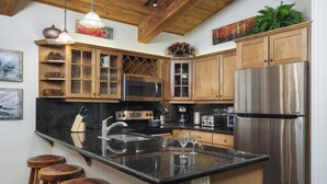 Eine Küche mit Holzausstattung, einem Edelstahlkühlschrank, einer Granitarbeitsplatte und Barhocker.