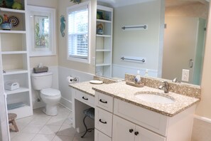Une salle de bain avec un double lavabo, des toilettes, des étagères et une fenêtre.