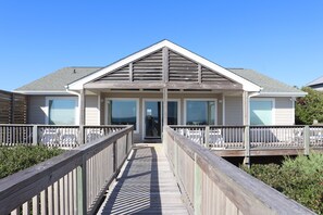 Une propriété située en bord de mer, dotée d’une allée couverte, d’une entrée principale et d’une grande fenêtre donnant sur l’océan.