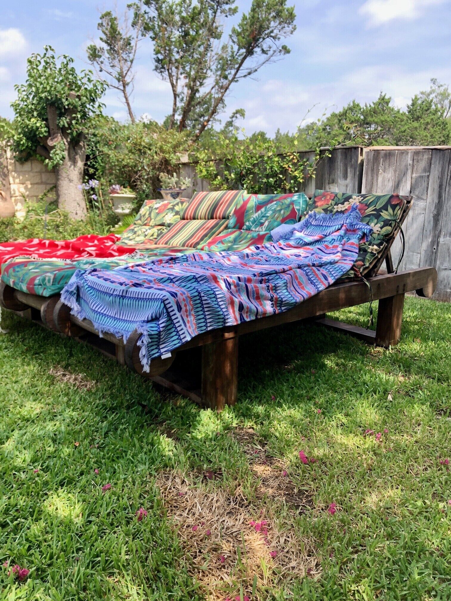A wooden bed with colorful bedding in a grassy outdoor setting.