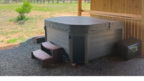 Un jacuzzi bajo una pérgola de madera con vistas a un patio cercado y árboles.