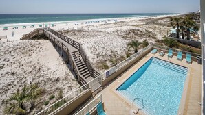 Ein Hotel direkt am Strand mit Swimmingpool, Strandliegen und einer Holzterrasse, die zum Strand führt.