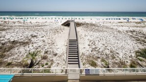 Ein Strand mit einer Promenade, die zum Wasser führt, einem Poolbereich und Strandsonnenschirmen.