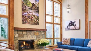 A cozy living room with a stone fireplace, large windows, and a blue sofa.