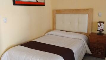 A hotel room with a large bed, a headboard, a nightstand, a wall-mounted painting, and a tiled floor.
