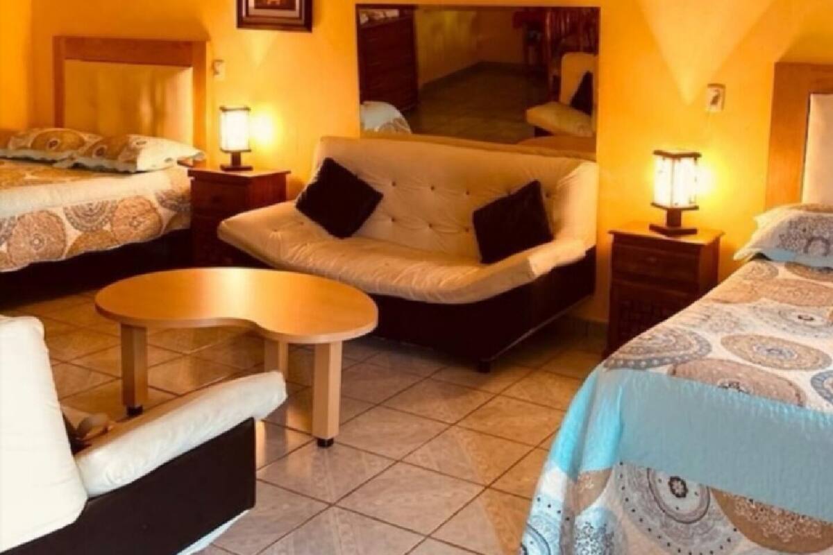 Una habitación de hotel con sofá cama, una mesita pequeña y dos mesitas de noche con lámparas.