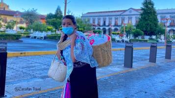 A person walking on a paved area with hexagonal tiles, carrying a woven bag and a handbag.