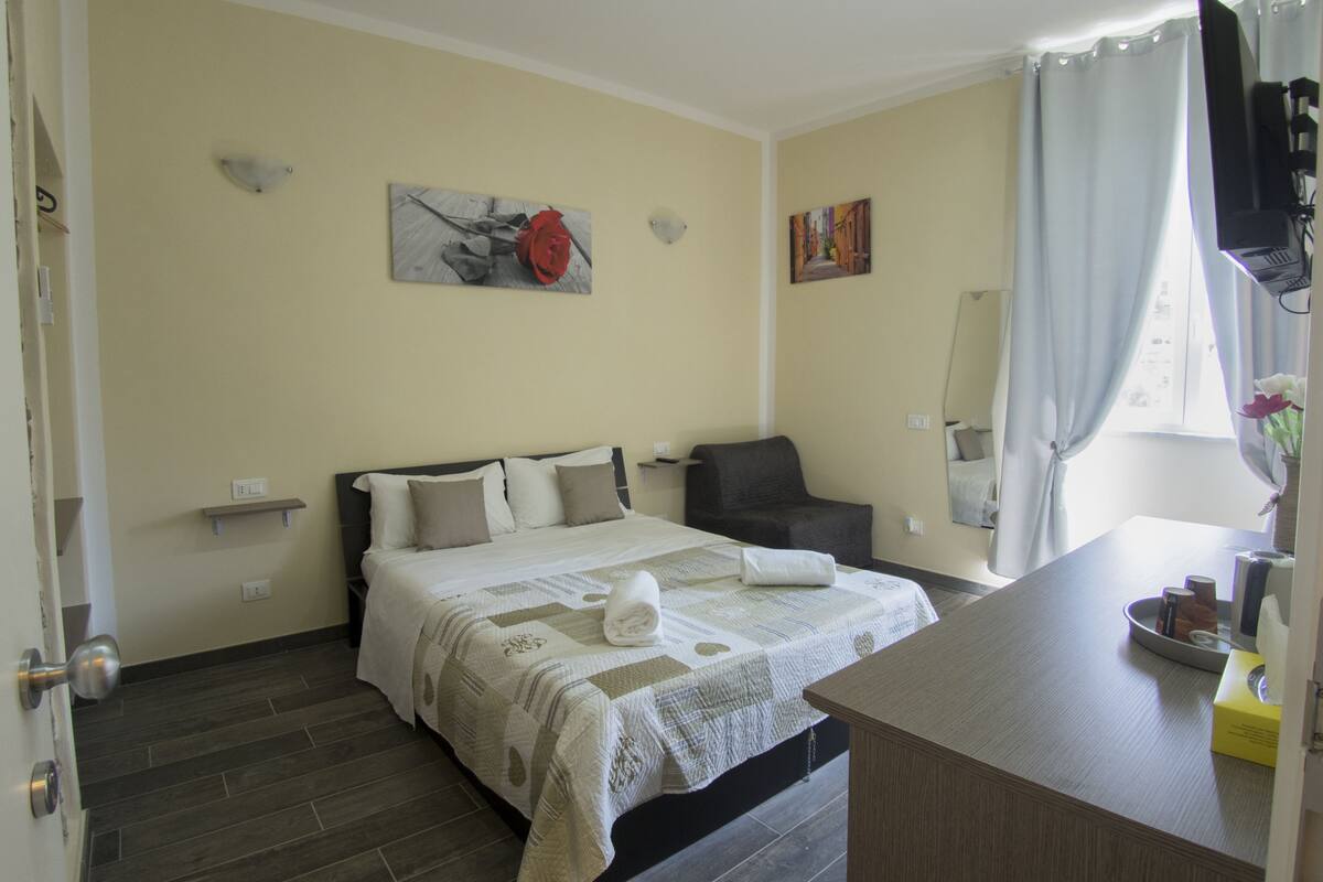 Ein Hotelzimmer mit Bett, Stuhl, Schreibtisch und einem fenster mit Vorhängen.