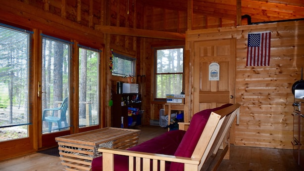 L’intérieur d’un chalet en bois, avec un banc en bois, une table et une porte ornée d’un drapeau américain.