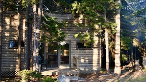 Une cabane en rondins dotée d’un porche, entourée de grands arbres et agrémentée d’une terrasse en bois.