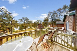A wooden deck with a glass table and chairs, overlooking a wooded area with cabins. - White Wing Resort (Branson)