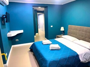 A hotel room with a bed, a nightstand, a lamp, and a television. - Napoli Centro (Naples)