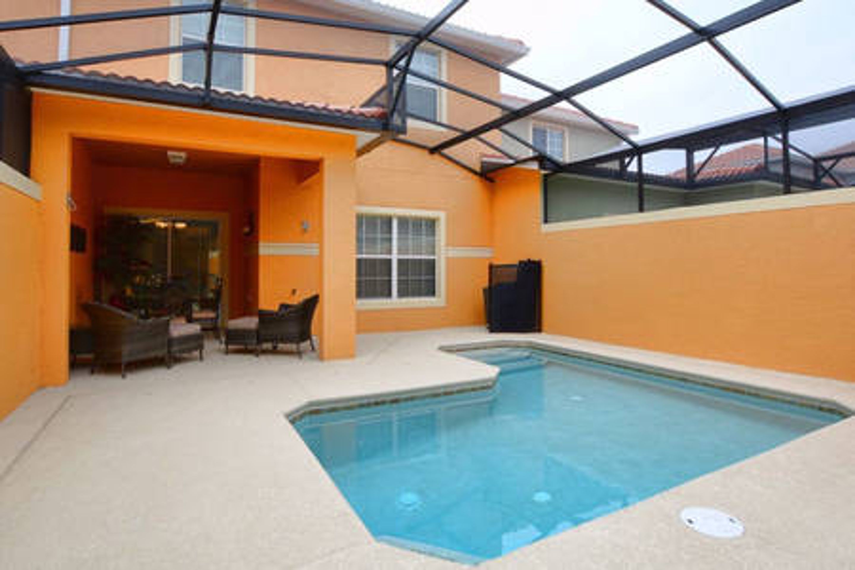 A swimming pool with a glass enclosure, surrounded by orange walls and a tiled deck.